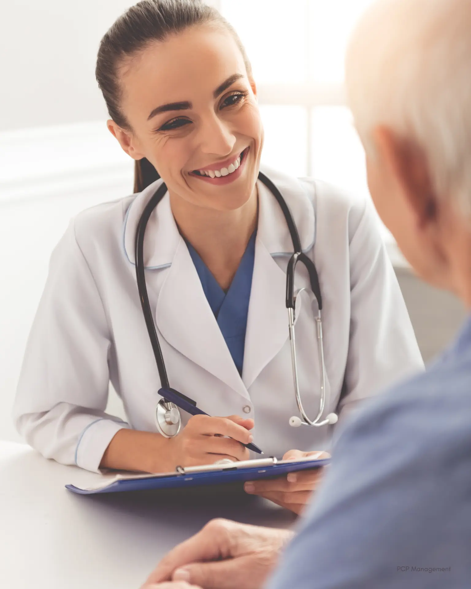 A physician talking with an older patient across a wooden table in a quiet private practice consultation room.